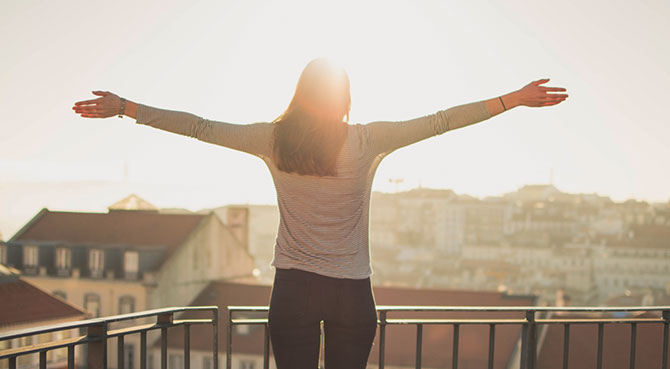 woman in recovery celebrates on balcony with arms open wide after discovering ways to get more energy naturally