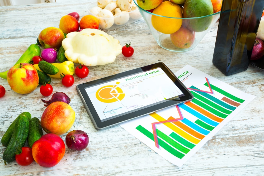 Nutrition Symbolized by Fruits and Vegetables on a Counter with an Electronic Tablet and Printed out Charts
