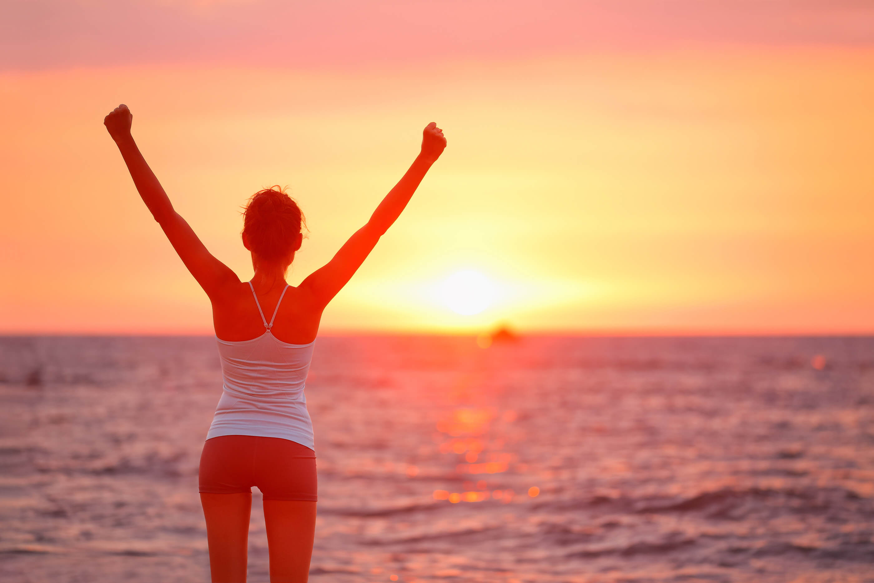 woman at beach with arms up celebrating national recovery month