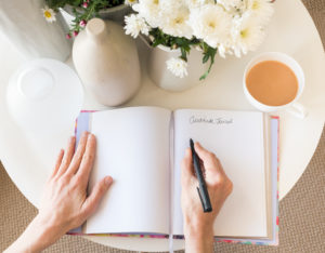 woman practicing mindfulness exercises by journaling in the morning with coffee