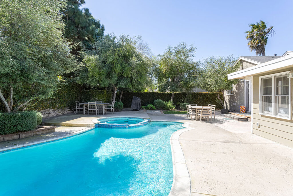 a beautiful, blue pool in a back yard surrounded by trees and greenery