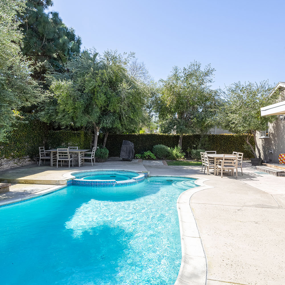 a beautiful, blue pool in a back yard surrounded by trees and greenery