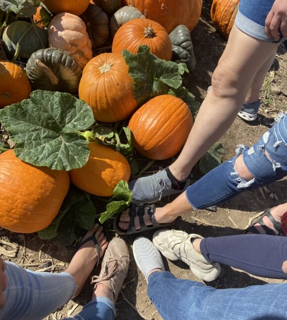 a group of friends in a pumpkin patch put their feet in a circle