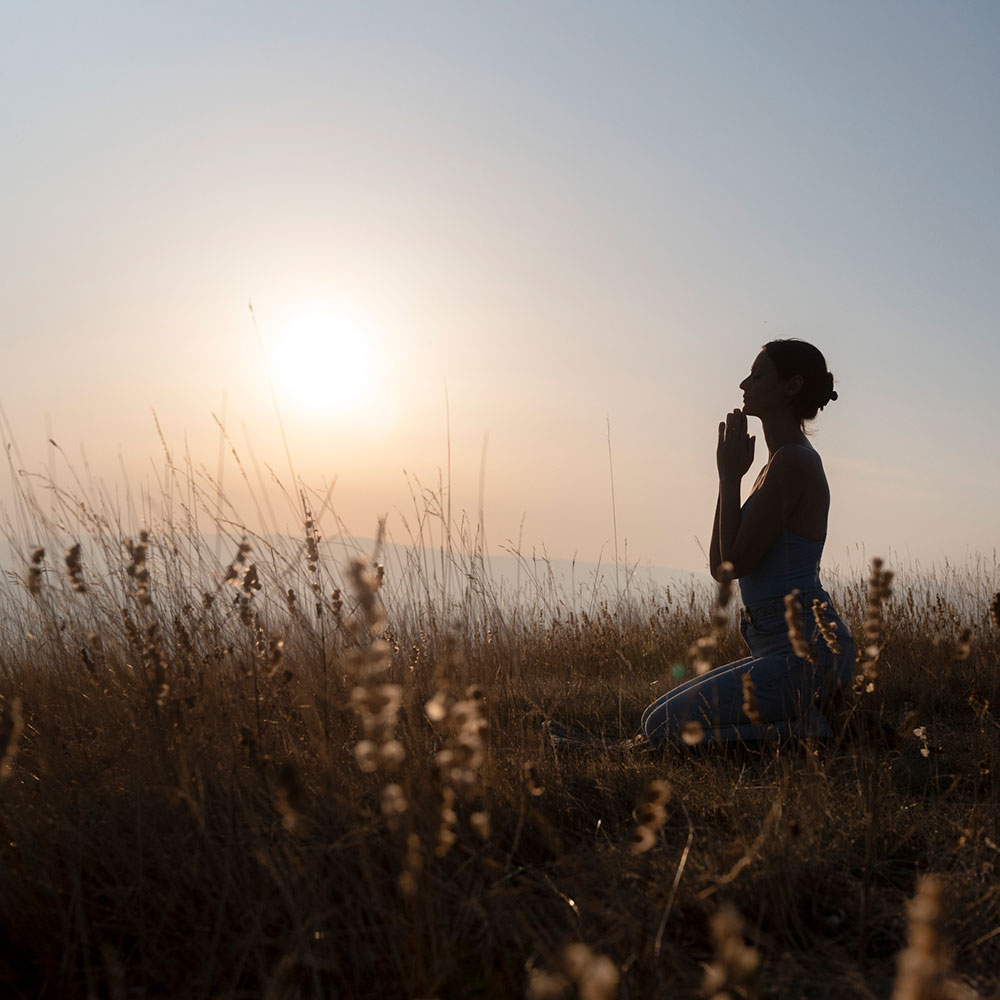 a woman kneeling in a field, with her hands pressed together