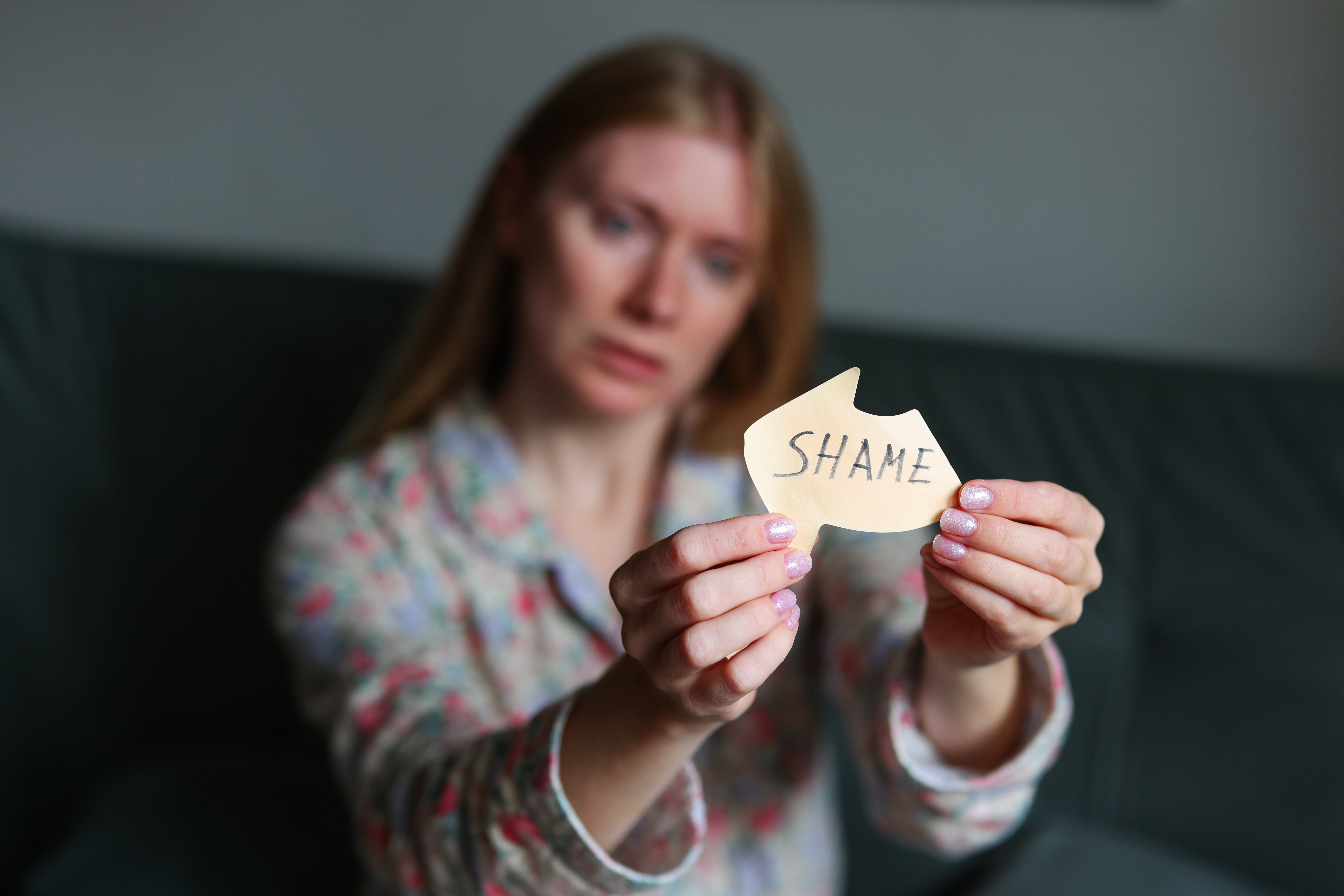 Woman holding paper with the word shame written on it.