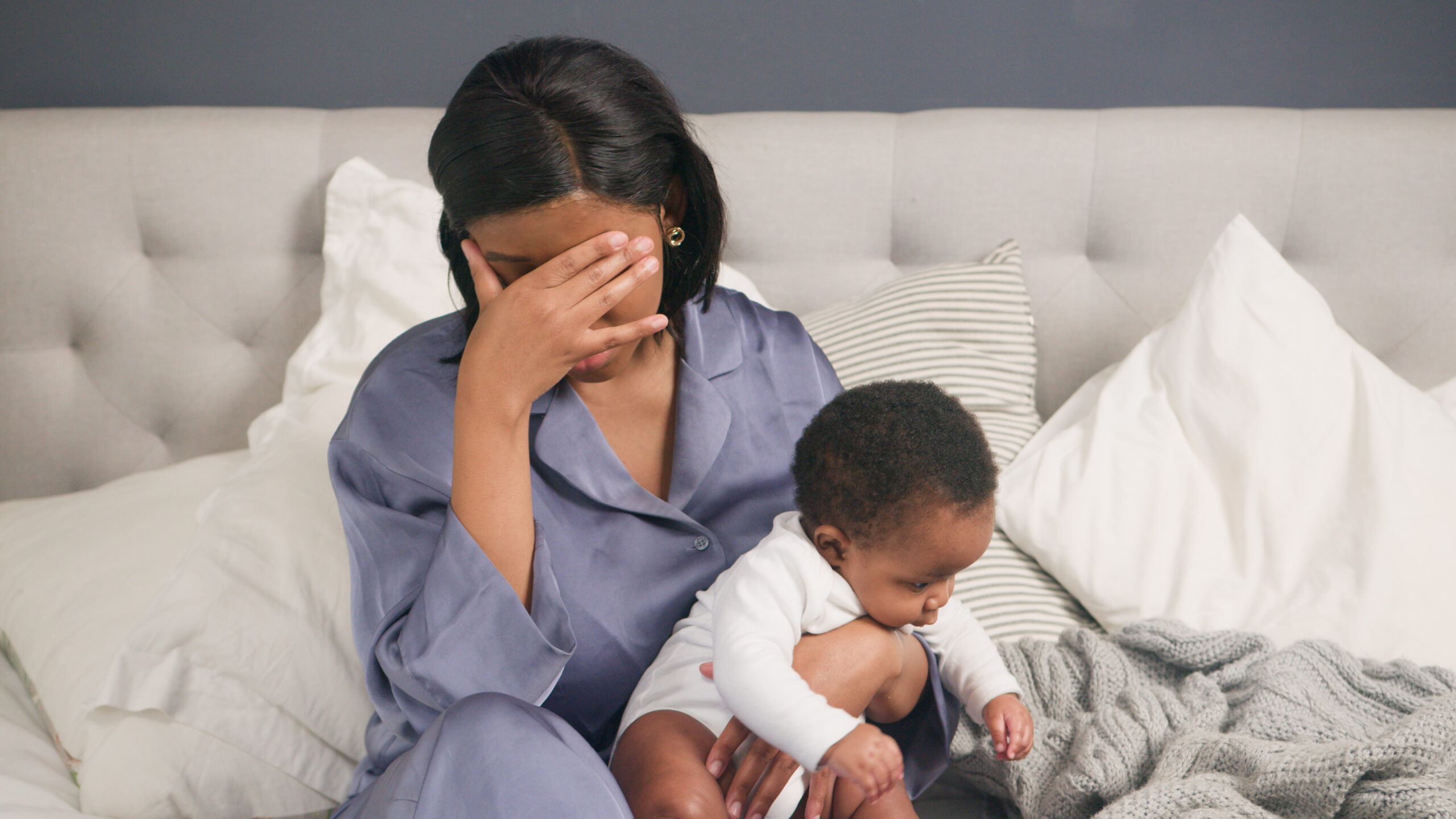 Tired mother holding baby and covering her face