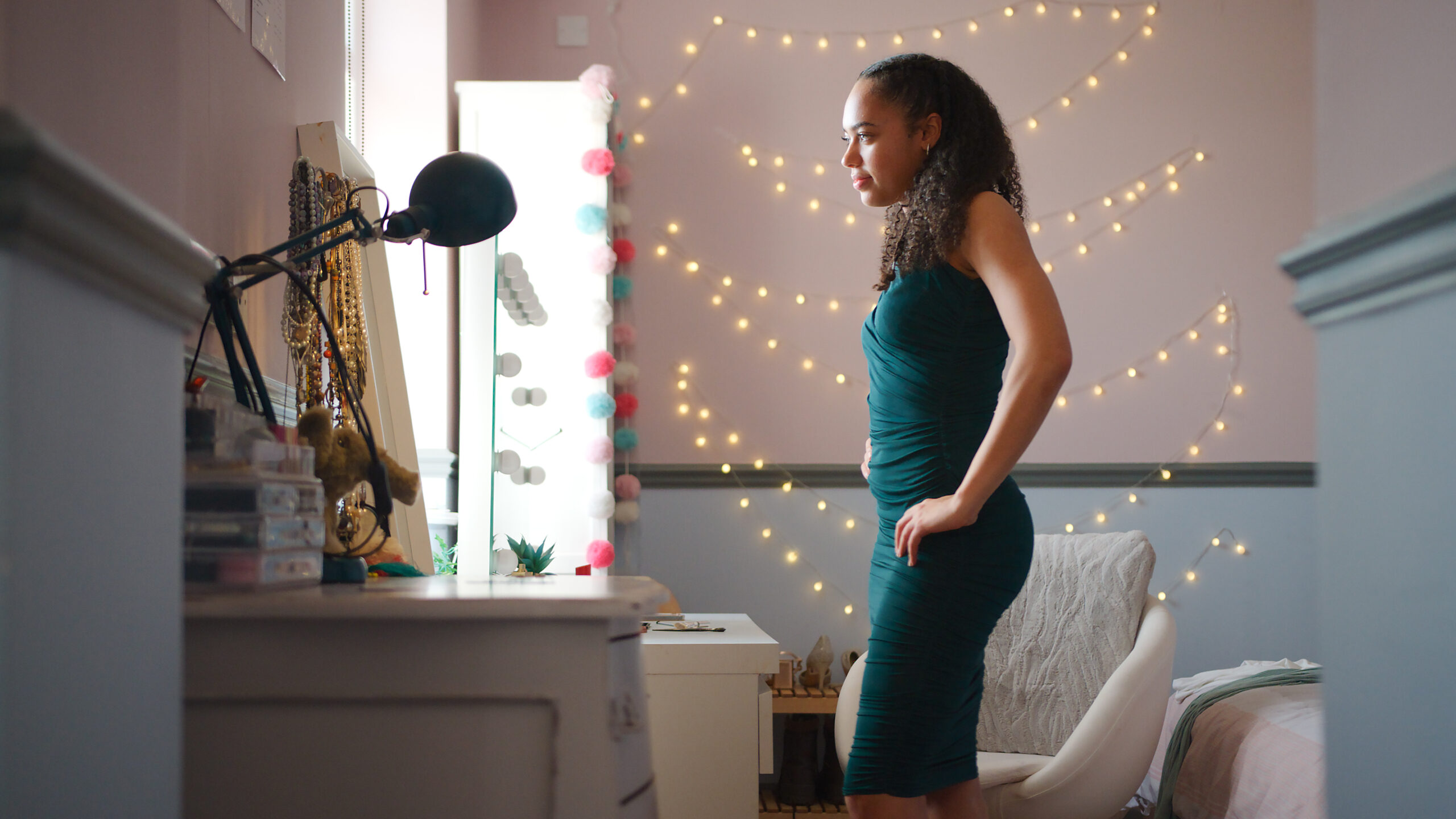 oung woman looking at herself in mirror with string lights behind her