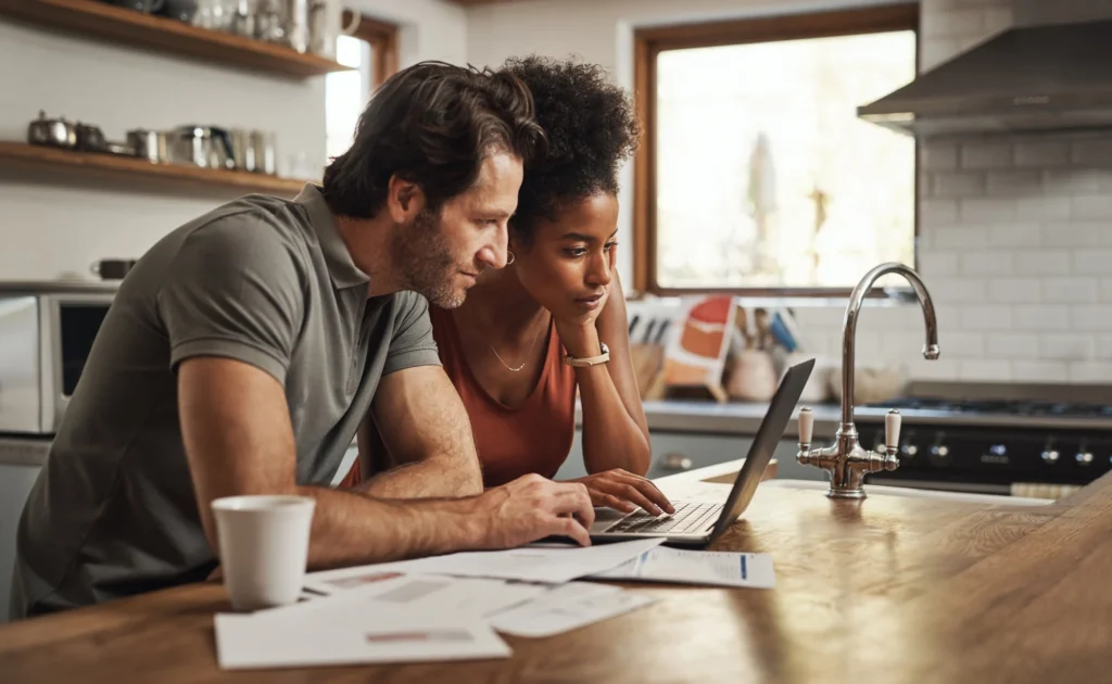 Two adults reviewing paperwork and a laptop at a kitchen table