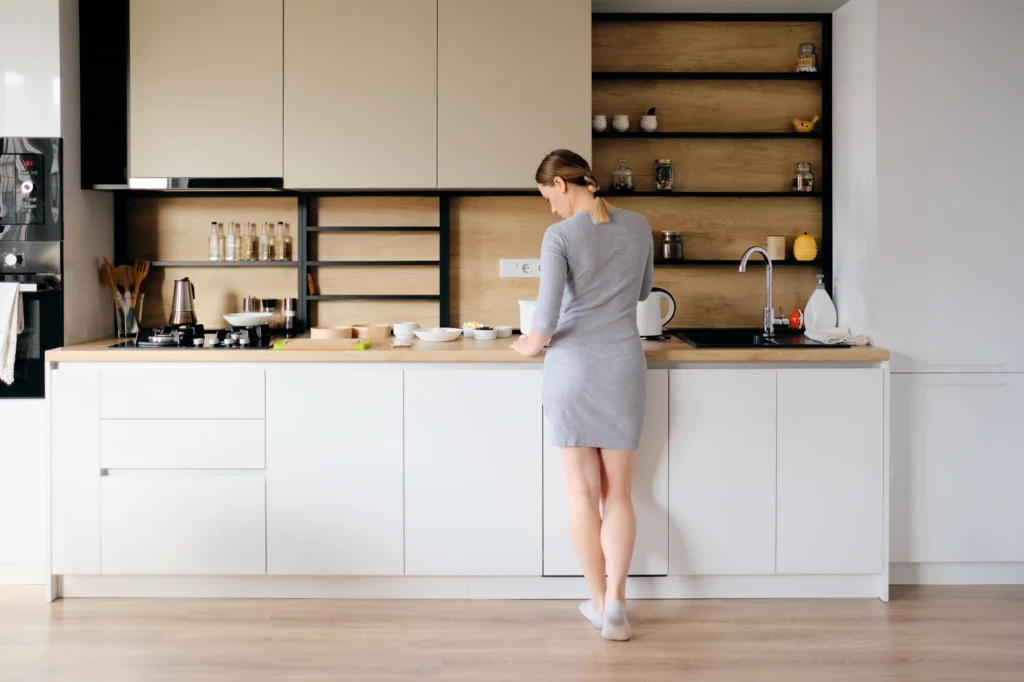 A woman standing alone in a home kitchen, leaning on the counter with a pensive expression