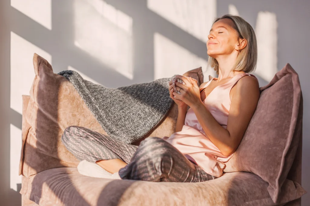 A woman sitting on a couch at home holding a mug of tea, looking off to the side in thought