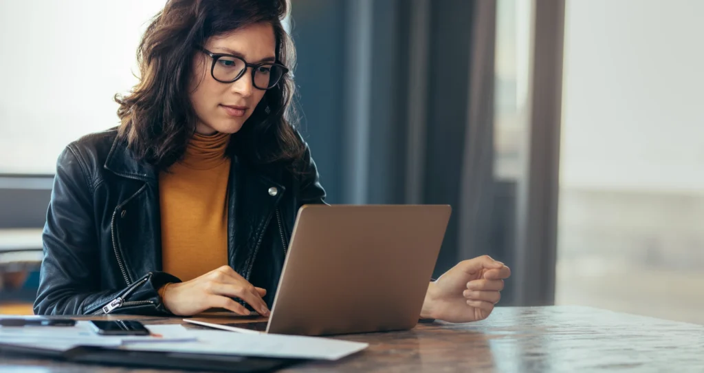 A woman sitting at a desk working on a laptop with a calm, focused expression