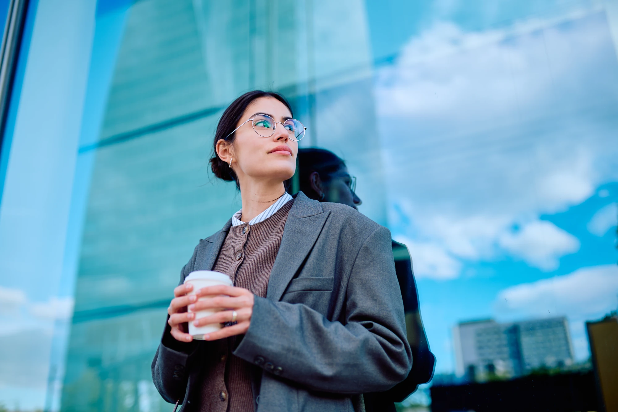 A woman standing outdoors glancing back over her shoulder with a guarded expression
