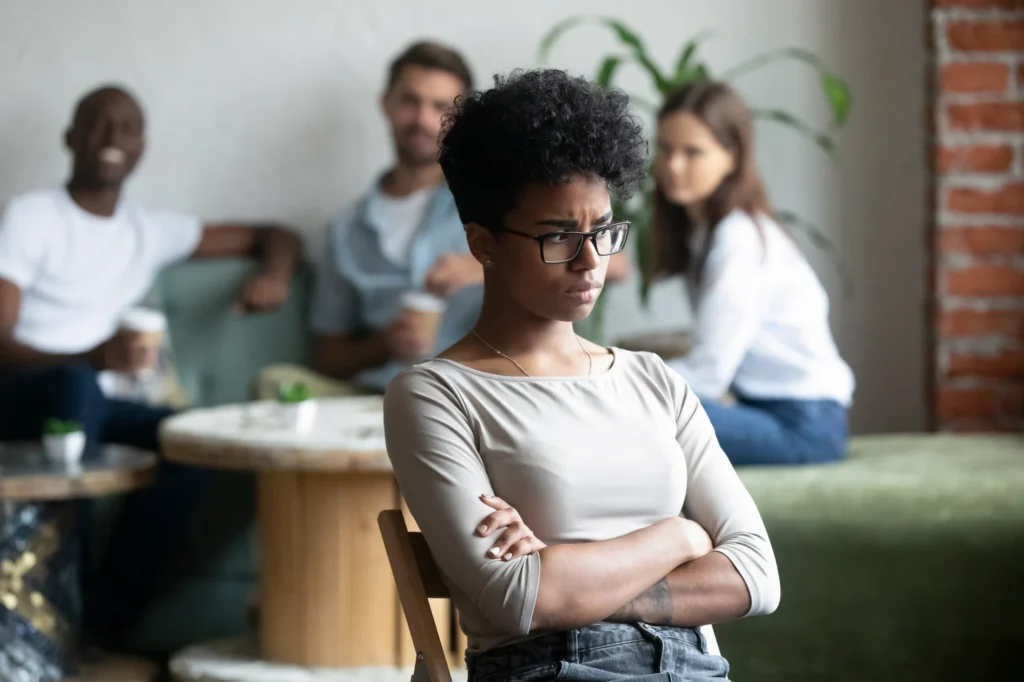 A woman sitting slightly apart from a group of friends talking together, looking withdrawn