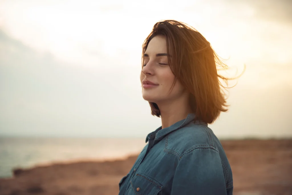 A woman standing on a beach with her back partly turned, looking out at the ocean