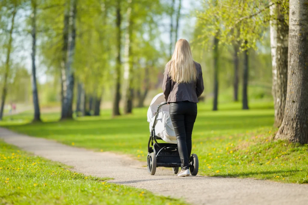 A woman walking outdoors on a sunny path, pushing a baby stroller