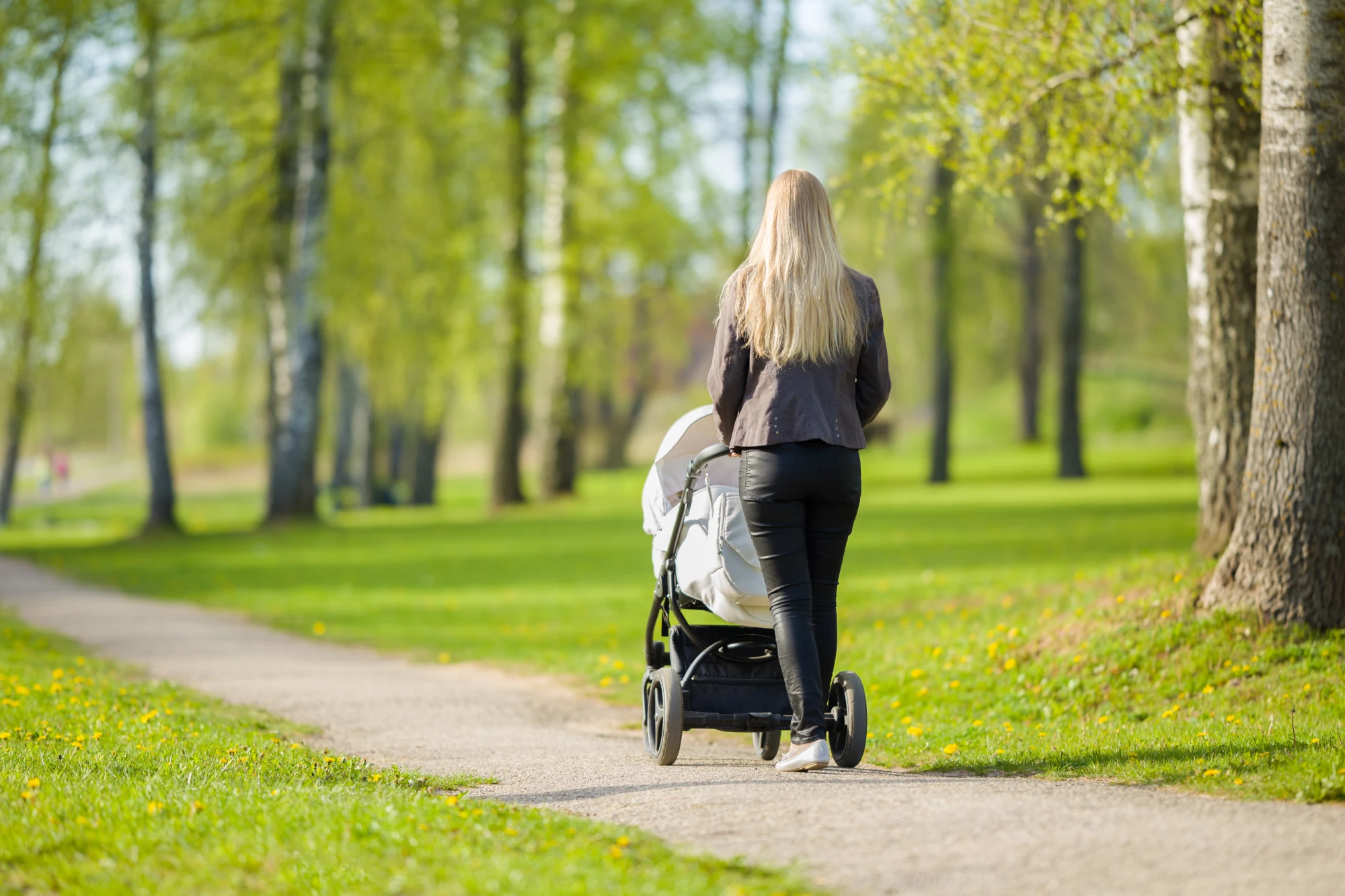 A woman walking outdoors on a sunny path, pushing a baby stroller