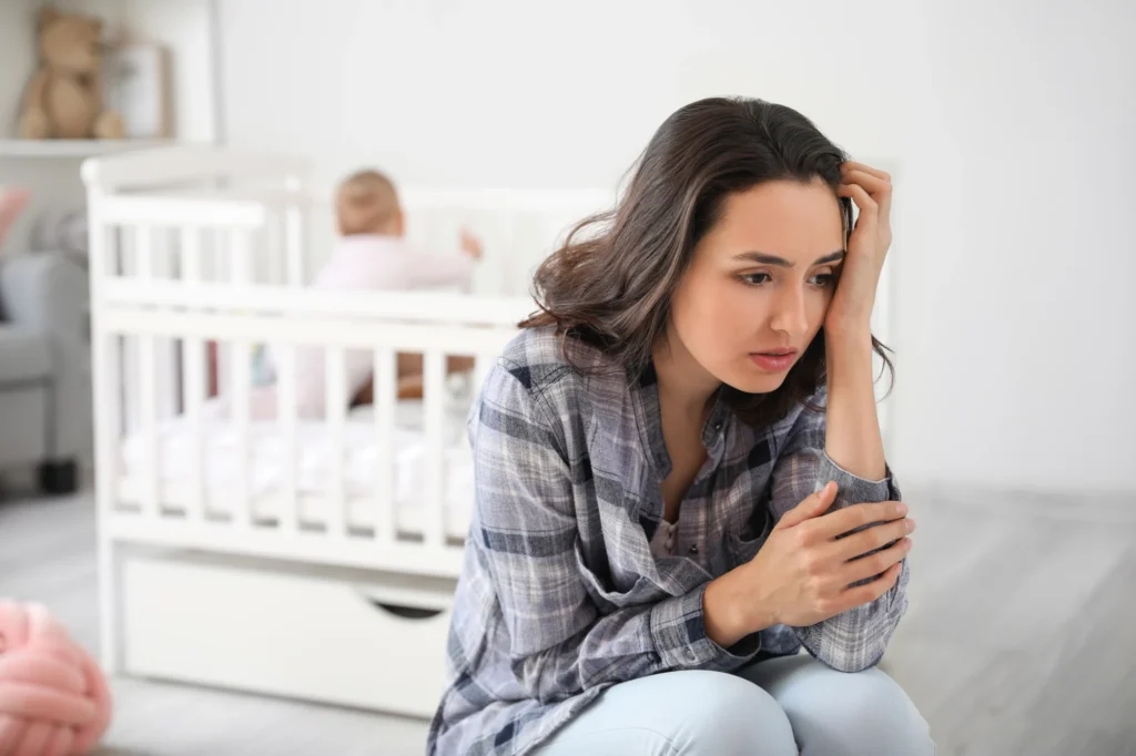 A tired mother sitting on a couch at home with her head resting on her hand