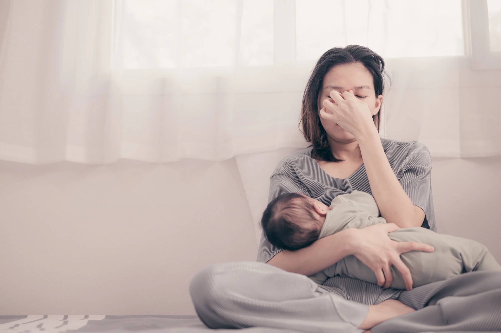 A new mother sitting at home holding her newborn baby with a thoughtful expression