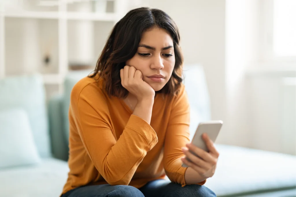 A woman sitting at home holding a phone to her ear with a concerned expression