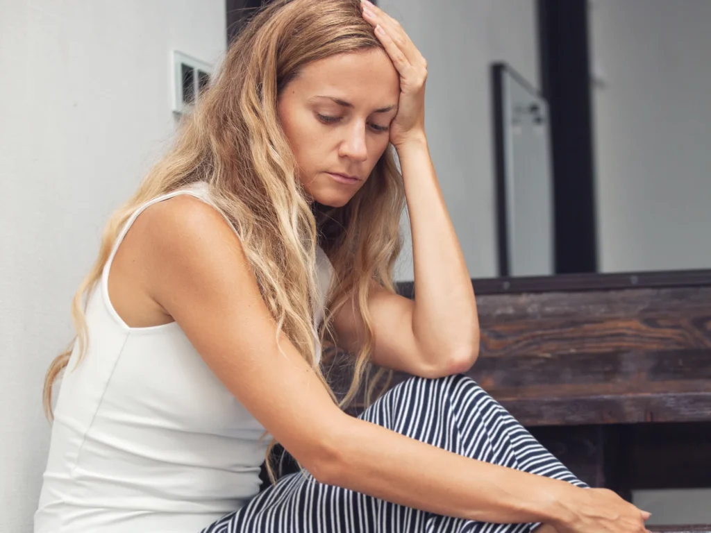 A woman sitting alone on a staircase at home, resting her arms on her knees and looking down
